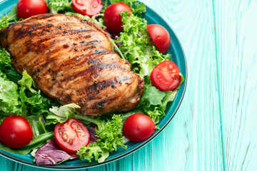 Grilled chicken breast ( fillet ) with lattuce salad and cherry tomatoes . Top view