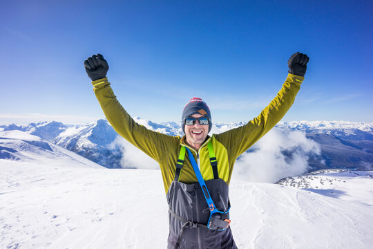 Man raises arms after successful winter ascent of mountain summit