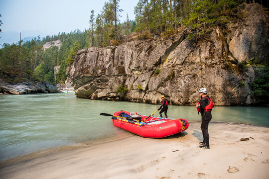 Two friends take a break on sandy beach during a river rafting trip.
