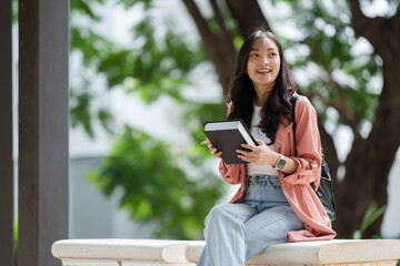 Obraz premium Outdoor pictures on the university campus Beautiful Asian girl Cute person holding a book or reading for knowledge and relaxing sitting outdoors.Learning concept.
