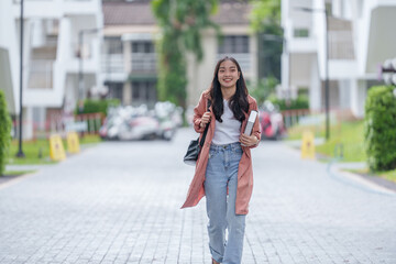 Portrait of a charming Asian female student in casual clothes. With backpack walking on campus her...