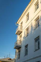 A minimalistic architectural photograph of a white building with balconies, captured in warm evening light. The simplicity of the design and soft shadows create a serene urban aesthetic 