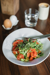 Bowl with tasty salad consisting of lightly salted salmon, arugula, cherry tomatoes, green beans, microgreens, avocado, seasoned with olive oil and lemon juice on wooden table.