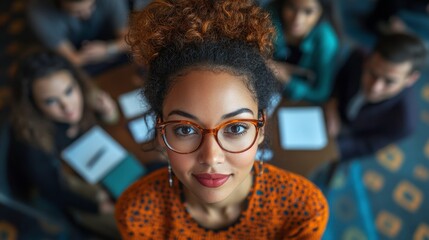 A woman with glasses looks directly at the camera, surrounded by a group in a meeting setting.