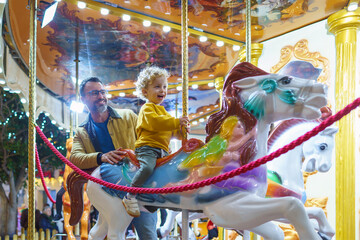 Father and son enjoying christmas carousel ride together