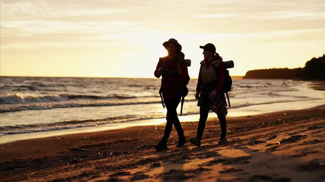 Traveling in nature, hikers admiring beautiful seascape in sunset, silhouette. People walking on coastline, enjoy freedom and beauty of nature, slow motion, cinematic shot with backers on seacoast