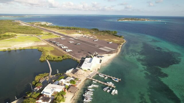 Los roques airport near turquoise caribbean waters and docked boats on a sunny day, aerial view