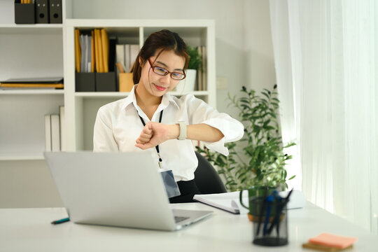 Asian female office worker sitting at her work desk and checking time on wristwatch