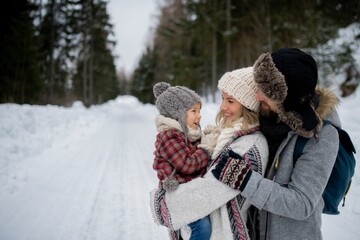 Young family is enjoying winter holiday in the mountains, standing in the middle of snowy forest.