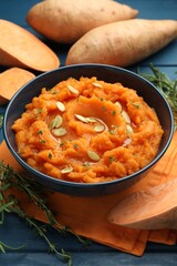 Tasty mashed sweet potato with pumpkin seeds in bowl, fresh vegetables and thyme on blue wooden table, closeup
