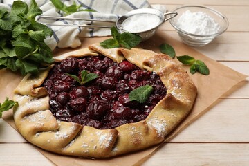 Tasty galette with cherries, mint and powdered sugar on wooden table