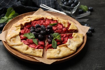 Tasty galette with strawberries, blueberries and mint on dark gray textured table, closeup