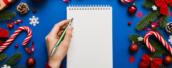 Woman writing Christmas to do list on notebook on colored background with xmas decorations