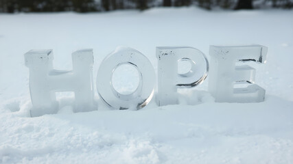The word "HOPE" arranged with letters carved out of crystal-clear ice, placed delicately on a soft snow surface
