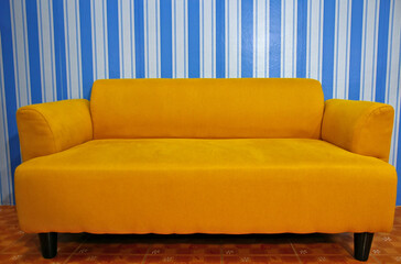 There is a simple yellow sofa placed in front of the blue striped wall.