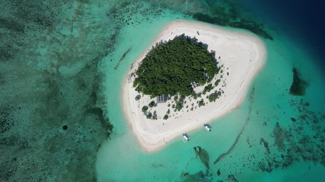 An aerial view of a small tropical island with lush greenery, white sandy beaches, and vibrant turquoise waters, located in Balabac, Philippines