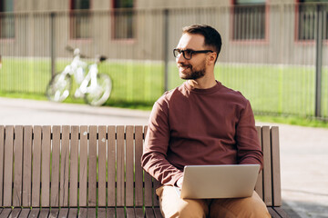 Portrait of happy, smiling bearded man wearing eyeglasses, using laptop, attractive student studying