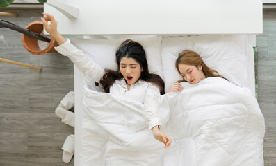 Young asian woman in white pajama, sleep and sweet dream lying with soft pillows and a comfortable duvet wrapped around. The other stretching while yawning in a white bed. Top view