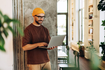 Handsome Hispanic businessman freelancer wearing stylish yellow hat and eyeglasses holding laptop
