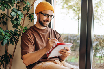 Portrait of smiling, happy, bearded man wearing stylish eyeglasses and yellow hat taking notes