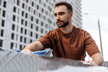Portrait of pensive handsome man wiping down white SUV with microfiber cloth at self-service station