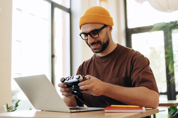 Portrait of smiling, handsome bearded man photographer holding camera using laptop