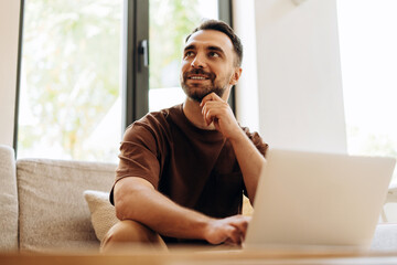 Portrait of smiling, handsome Latin man, freelancer, copywriter typing on keyboard, using laptop