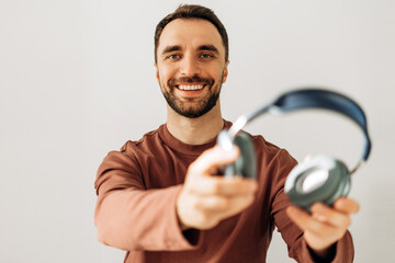 Portrait of happy, attractive beaded man holding earphones, showing, looking at camera