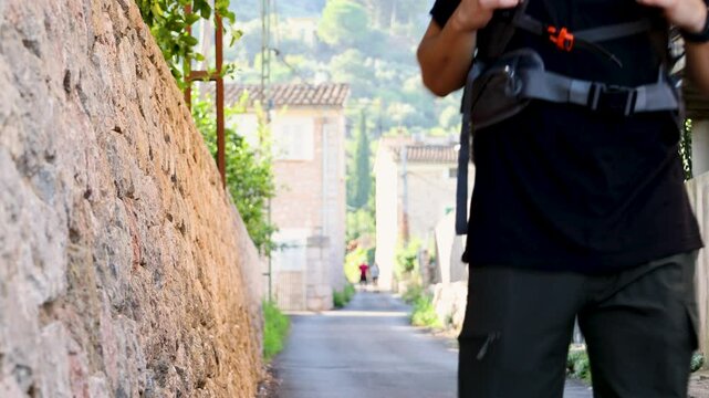 Cheerful traveler man walking in nature with backpack in a village with green mountains in background on a sunny day, backpacker and explorer concept