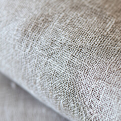 Close-up of natural fabric texture showcasing the details of fiber weaving with soft light in the background.

