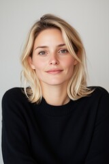 Fototapeta premium A beautifully composed portrait of a young blonde woman wearing a black sweater, posing with a calm and confident expression against a softly textured light background,with copy space.