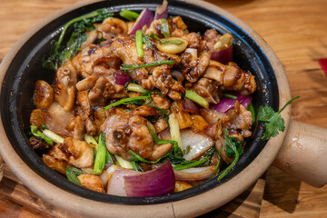 A clay pot dish filled with braised chicken, garlic, onions, green onions, and herbs, all seasoned with a savory sauce in Sanya, Hainan, China