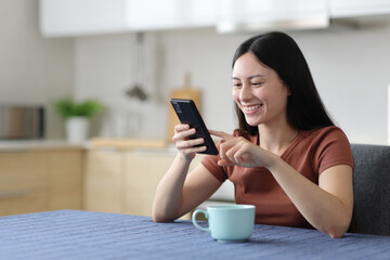 Happy asian woman checking cell phone in the kitchen