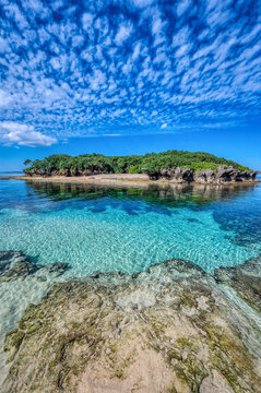 Crystal clear waters of Bise Beach, Motobu District, Okinawa main island. White sand beach with coral outcrops and small islands offshore.