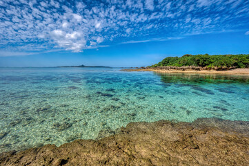 Crystal clear waters of Bise Beach, Motobu District, Okinawa main island. White sand beach with coral outcrops and small islands offshore.