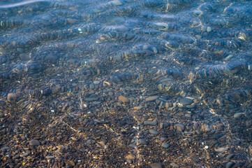 Underwater pebble backgrounds. Colorful stones sea bottom in the sun rays. View from above through clear water. Seascape wallpaper texture. Defocus.