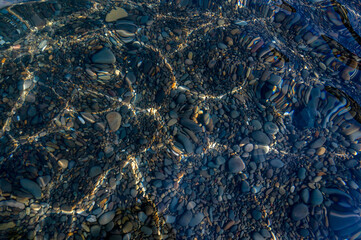Underwater pebble backgrounds. Colorful stones sea bottom in the sun rays. View from above through clear water. Seascape wallpaper texture. Defocus.