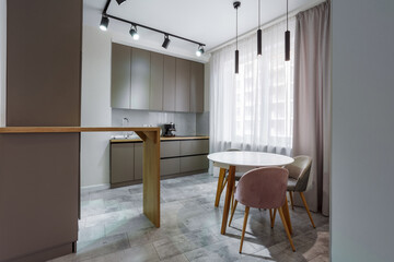 Modern kitchen in a small cozy contemporary studio apartment. Table and chairs in the foreground. Built in household appliance