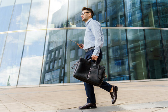 Professional man walking in urban setting, carrying briefcase and using smartphone during daytime