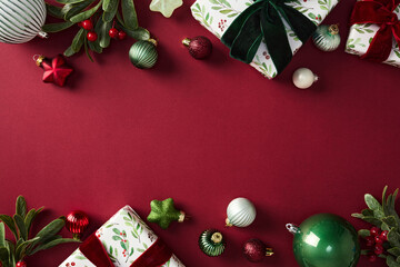 Stylish chic Christmas decorations and gifts on red backdrop, featuring baubles, bells, and wrapped...