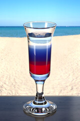 Multi-layered liquor on the wooden table in the beach bar. Picturesque background with sand and sea. Glassware with the drink. Pousse cafe glass. 3d rendering.