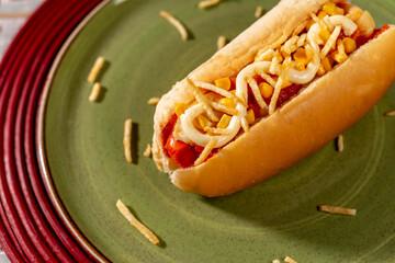 Brazilian Hot dog on green plate with corn and mayonnaise and crispy fries.