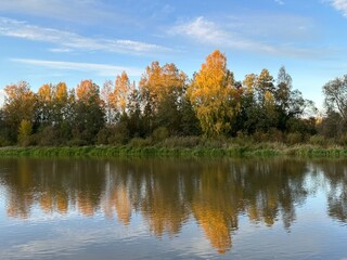 Sunlit autumn trees reflected in the water of Emajõgi river in Supilinn, Tartu, Tartumaa, Estonia, October 2023