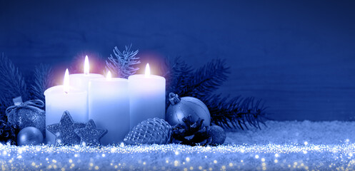 Four burning Advent candles on white snow isolated on blue background.
