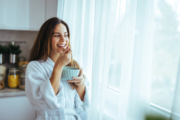 Woman Enjoying Breakfast Cereal By Window In Cozy Morning Robe