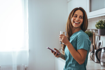 Smiling Nurse Holding Phone and Glass in a Bright Kitchen