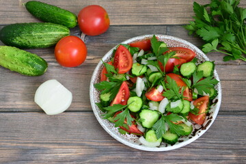 a bowl of vegetables, cucumber, tomato and parsley on a wooden table 