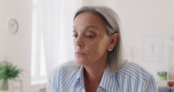 Gray haired senior woman expresses displeasure and disappointment. Old lady with bob haircut, in striped shirt, with serious displeased angry disappointed face expression looks at camera and then away