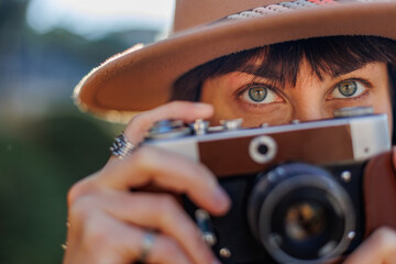 Fashionable look, young woman with a film camera wearing an elegant hat and coat. A hipster tourist...