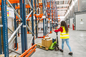 Warehouse young female worker moving boxes with pallet jack in logistics center